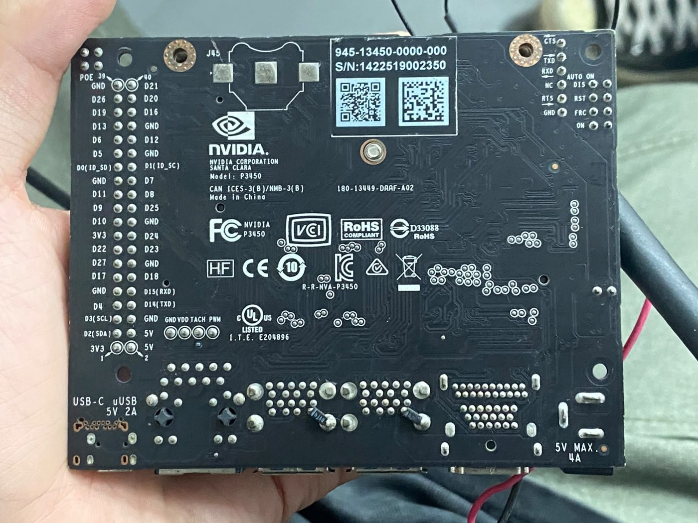 The underside of a Jetson Nano developer kit held in a hand, showing the NVIDIA P3450 model marking, the 40-pin header labels and the 5V 4A barrel jack marking.